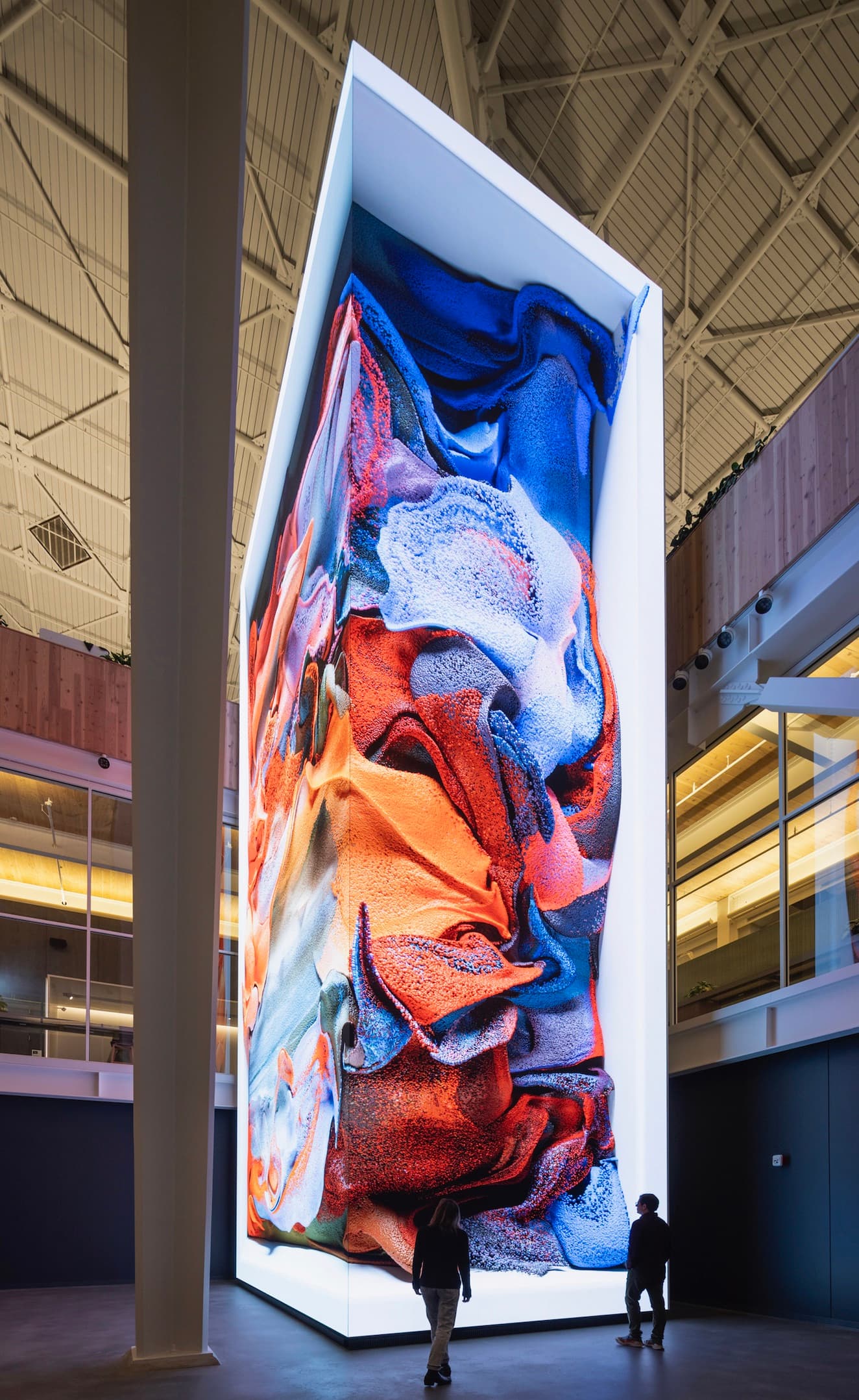 Visitors viewing a tall digital installation with red and blue folded forms